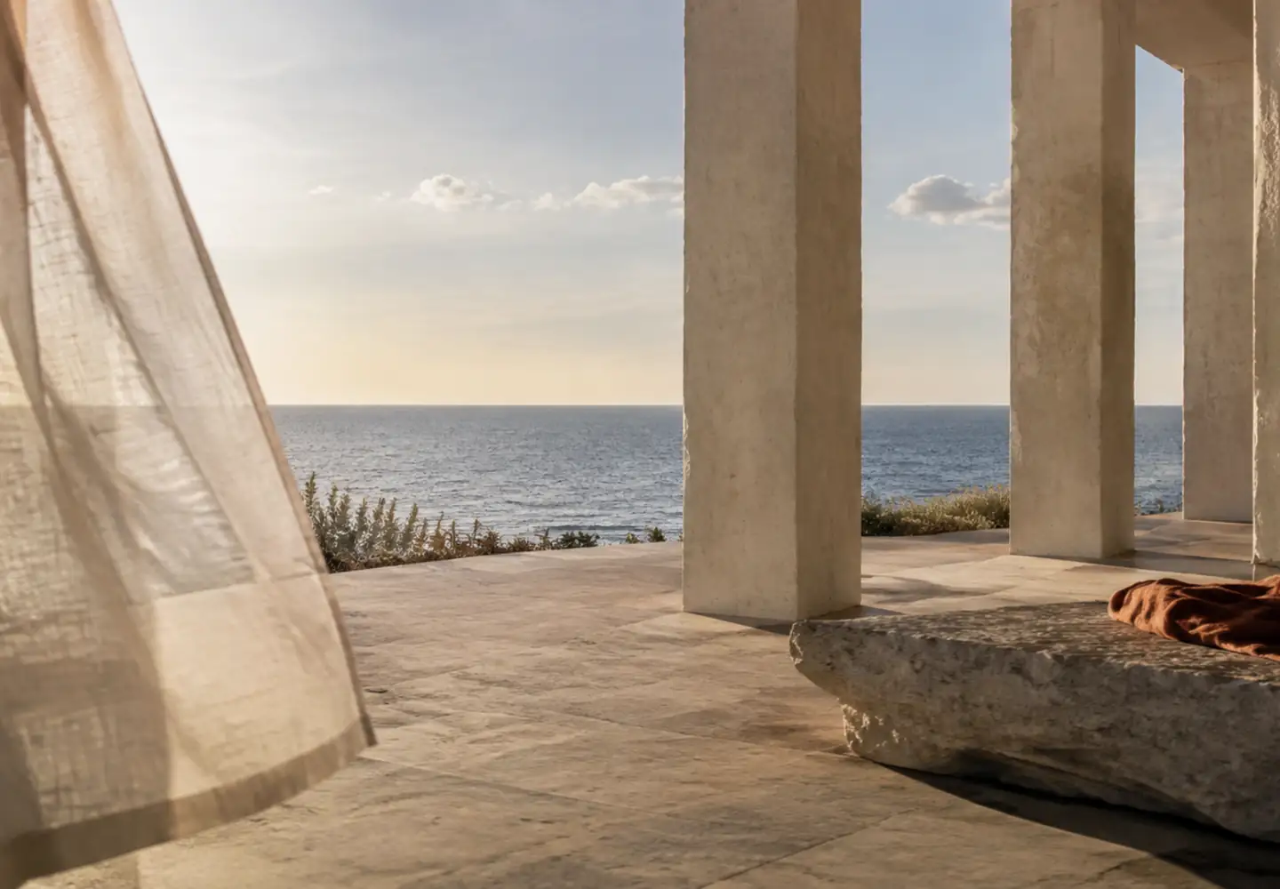 Logia de piedra frente al Atlántico con columnas rítmicas y una cortina de lino movida por la brisa